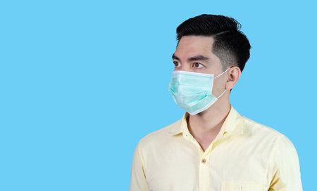 COVID-19 Coronavirus close up handsome young asian man wearing yellow shirt holding tablet and mask protection from covid 19 isolated on white background in studio. Asian man people.の写真素材