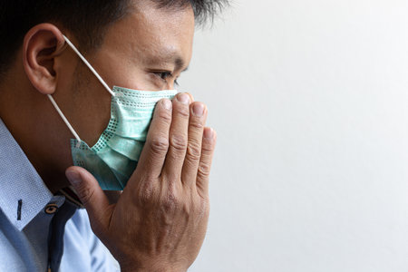 The young man has headache coughing and sneezing which is caused by the infection of the COVID-19 virus or the CORONA virus By wearing a mask to prevent the germs from spreading to those around you, Hygiene and Sanitation concepts.の写真素材