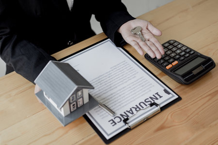 Real estate agent holds the keys to send to the client and offers the conditions for signing the house sale agreement and home insurance to the client, Home sales and home insurance concept.の写真素材