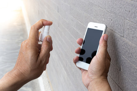 Men use alcohol spray to get rid of bacteria and viruses on mobile phones, Inhibition and prevention of Covid-19 virus infection using 70 percent alcohol, protect virus concept.の写真素材