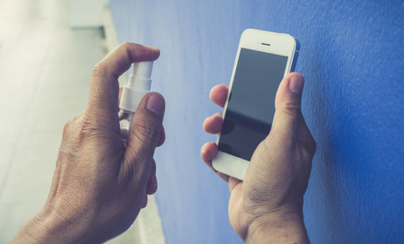 Men use alcohol spray to get rid of bacteria and viruses on mobile phones, Inhibition and prevention of Covid-19 virus infection using 70 percent alcohol, protect virus concept.の写真素材
