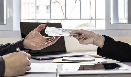Businessmen give dollars to bribe employees in signing contracts to buy illegal land and real estate, Business fraud and social injustice, corruption and bribery concept.の写真素材