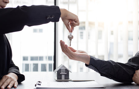 Sales manager or real estate agent holds the key handing it to the customer after signing the house purchase contract with home insurance, Trading of mortgages and insurance concept.の写真素材