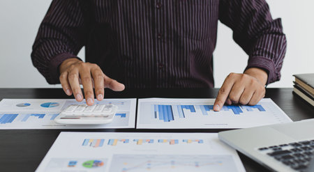 Accounting businessmen are calculating company income tax with calculators and graphs on the desks,...