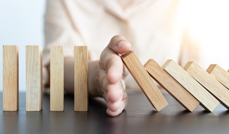 Businesswoman stops hands falling over domino to stop risk continuously, Continuous damage reduction, Stop business domino failures concept.の写真素材