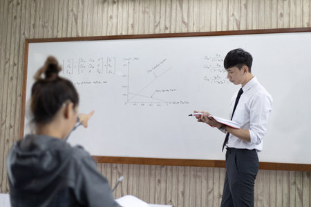 Teacher is teaching physics to students during the new school days after a long break, High school student classroom, Teacher is writing the instructional formula and explains how to do the exercises.の写真素材