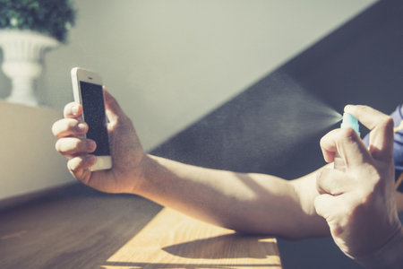 Close up young Asian man's hand is spraying an alcohol spray to kill germs on smartphones, Initial protection against germs, Cleaning of electronic appliances or disinfectants during an epidemic.の写真素材