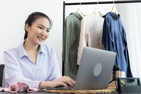 Young Asian woman chatting with a bright smile to a customer who wants to buy her clothes online with a laptop and confirms the order to close the deal, Social media trading or online shopping.の写真素材