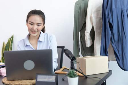 Young Asian woman chatting with a bright smile to a customer who wants to buy her clothes online with a laptop and confirms the order to close the deal, Social media trading or online shopping.の写真素材