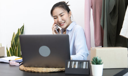 Asian businesswoman is taking online orders from a phone and chatting with customers to confirm their order, Online clothing sales business, Business of selling clothes on social media or selling online.の写真素材