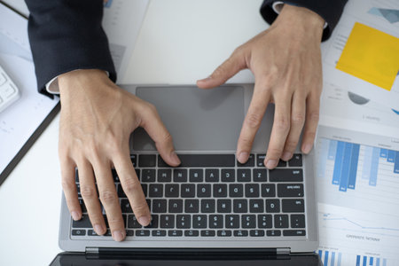 Young Asian office worker presses he finger on a laptop keyboard to analyze financial data and summarize her work in a private office, Office workers, handsome male employee in a black suit.の写真素材