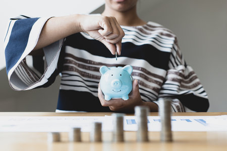Businesswoman's hand holds money or coins into a piggy bank, Managing money or saving money for future use, Saving for investment, Saving money for business growth or long-term profitability.の写真素材