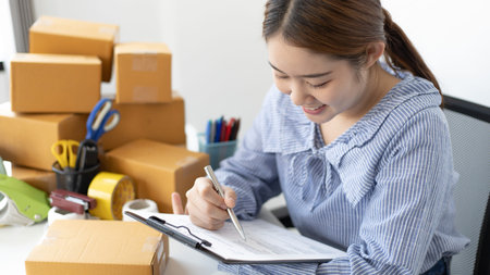 Young Asian woman is writing down the customer's details and addresses on the Clipboard in order to...