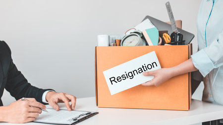 Employee handed over a document envelope and a box of work equipment beside him, Woman submits resignation documents to their supervisor and take personal equipment in a brown box from the office.の写真素材