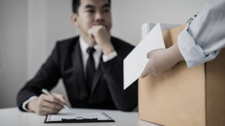 Employee handed over a document envelope and a box of work equipment beside him, Woman submits resignation documents to their supervisor and take personal equipment in a brown box from the office.の写真素材