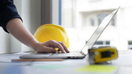 Young man with a laptop plotting a system of building structures in blueprints, Architects or...