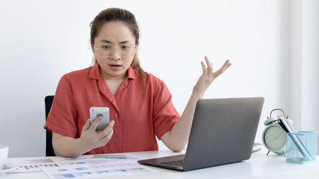 Asian female employee talking on the phone and working in a laptop with a Shock face, Office staff...