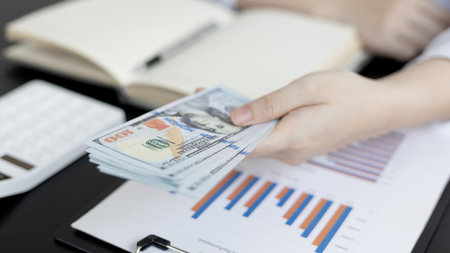 Give money, Young Asian business woman sits on a desk holding a dollar banknote preparing for a company employee, Payment under the terms of the company's treaty, Payroll concept.の写真素材