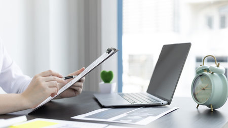 Asian business women are analyzing graphs, financial statistics and calculating corporate returns in...