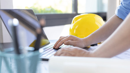 Young man with a laptop plotting a system of building structures in blueprints, Architects or...