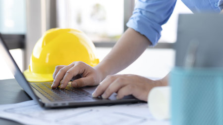 Young man with a laptop plotting a system of building structures in blueprints, Architects or...