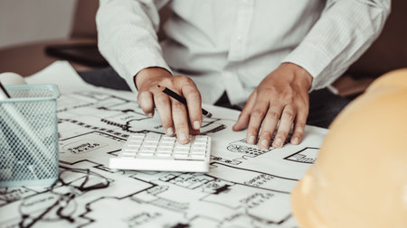 Male engineer or architect is pressing a calculator to calculate the building's structure and...