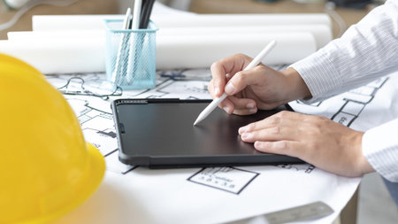 Young man using tablet plotting a system of building structures in blueprints, Architects or engineers are designing buildings using tablet to calculate the physical structure to be correct.の写真素材