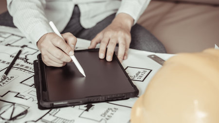 Young man using tablet plotting a system of building structures in blueprints, Architects or...