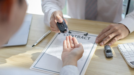 Car purchase contract and insurance, Man attendant handed over the car key to the customer who signed the contract and the terms of the agreement on the document.の写真素材