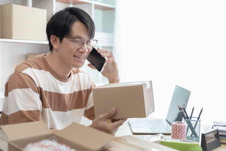 Asian man is taking online orders from a phone and chatting with customers to confirm their order, Selling products online or doing freelance work at home, Working at home and owning businesses.の写真素材
