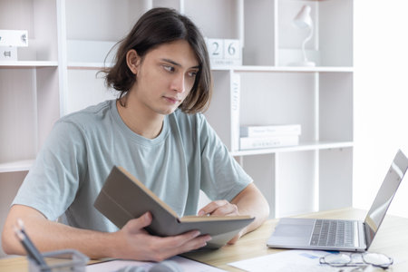 Asian man taking notes in notebook while studying online in laptop at home, Video chat, Online...