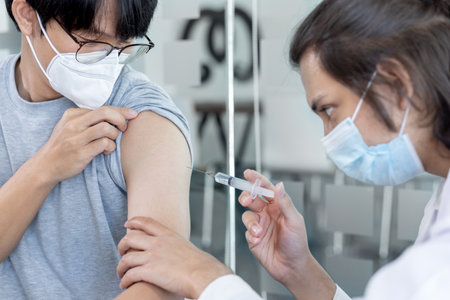 Doctor vaccinating patient, vaccination against new strains of virus, Doctor holding a syringe, Antivirus vaccination for people, Covid-19, Doctor vaccinating male patient in clinic or hospital.の写真素材