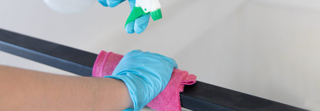 Young Asian male employee uses a towel soaked in alcohol to wipe off the railing or porch, Pathogen...
