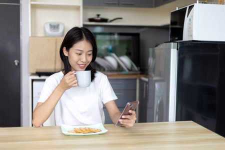 Asian woman eats breakfast with crackers (Healthy whole grain) and juice, Use your phone or mobile...