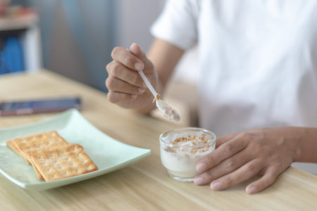 Half-Japanese woman eats yoghurt with cereal for breakfast in room, Healthy food and digestive system maintenance, The most popular and easy to eat breakfast food.の写真素材