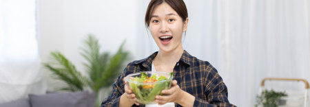 Asian woman eating salad on the dining table smiling and happy, Vegetable salads are rich in vitamins and minerals, Fat-low-calorie and high-fiber diets, Health care by eating fresh vegetables.の写真素材