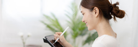 Asian woman taking notes in notebook while studying online in laptop or tablet  at home, Video chat, Online communication , Stay home, New normal, Distance learning
, Social distancing, Learn online.の写真素材