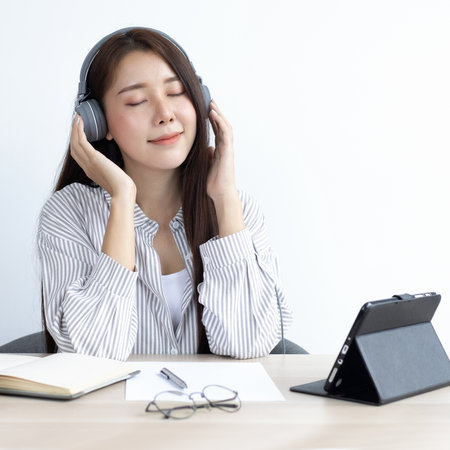 Young Asian woman happily listening to music in her private office, Relaxation by listening to music, Feel good concept.の写真素材