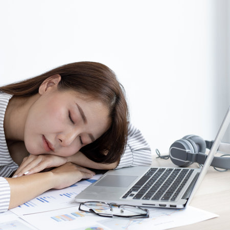 Financial accountant works on analyzing and summarizing the company's incomes and expenses in real estate and account management, causing her to get tired and fall asleep on her desk, Hard work and overtime work concept.の写真素材
