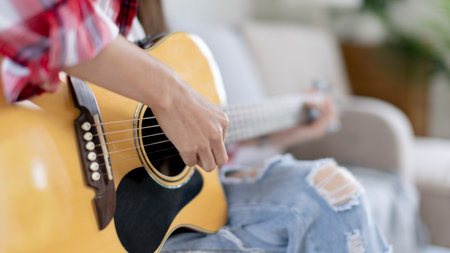 Woman practicing or learning to play guitar and practice using his fingers to hold guitar chords while looking at music notes with intention, Taking advantage of free time, Relax during free time.の写真素材
