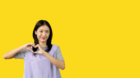 Asian young woman with bright smile making heart symbol shape with hands, Symbol of love and...