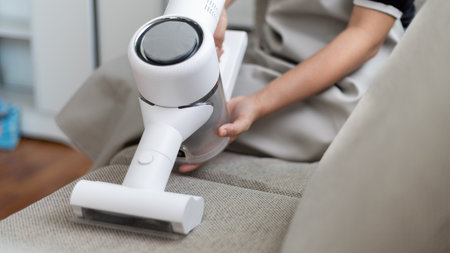 Beautiful woman vacuuming the sofa and pillow of her living room, Big cleaning in the house, Removes germs and dirt and deep stains, Housewife cleaning, Keeping her home clean, Domestic hygiene.の写真素材