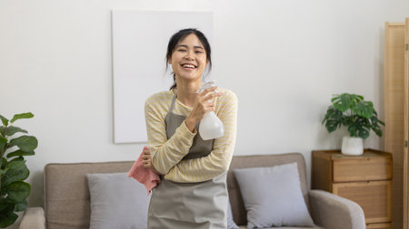 Asian housewife wearing apron holding rag and cleaning spray prepares for a big cleanup in the house, Housework, Daily routine, Big cleaning, Deep stain remover, Clean up on weekends.の写真素材