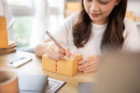 Woman Writing Customer Details for Shipping in Home Office, Packing Box and Writing Customer Information for Efficient Shipping, E-Commerce and Online Selling Concept.の写真素材