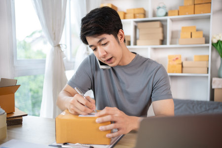 Man Writing Customer Details for Shipping in Home Office, Packing Box and Writing Customer Information for Efficient Shipping, E-Commerce and Online Selling Concept.の写真素材