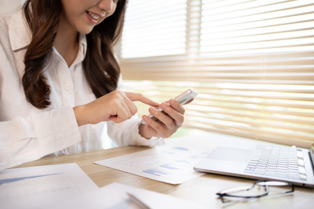 Young women use smartphones to play games or watch video clips to relax after a break from completing homework. Use mobile phones to create entertainment and happiness.の写真素材