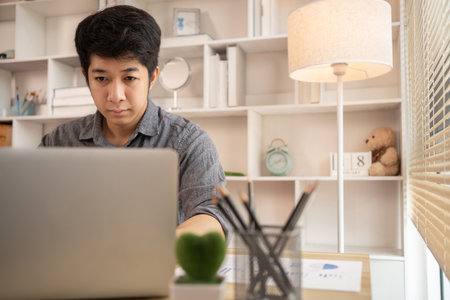 Man sat typing away on a laptop in his office with a determined look on his face, Work from the comfort of home, Male hand pressing on laptop keyboard, Work from home.の写真素材