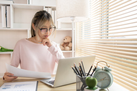 Work from home, Young woman analyzes data graphs on laptop and works intently in his personal office, Holding documents, Use your laptop for work and communication,の写真素材