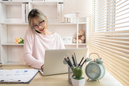 Young woman Multitasking: Typing on Laptop and Talking on Phone at Home Office , Home Workspace, Young woman who has a lot of work and is very busy with work.の写真素材