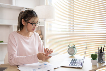 Young Businesswoman presses a calculator to calculate income tax and corporate income in a private office, Statistical graphs of investing in real estate, Finance, Accounting, Tex, Work for home.の写真素材